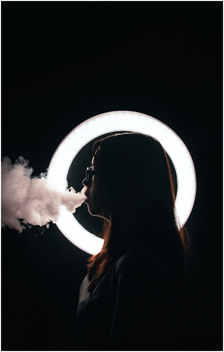 A girl backlit by a ring of white light, blowing vapour out to the left of the image.