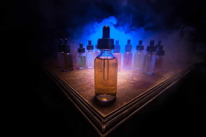 A bottle of vape liquid in front of a smoke screen.